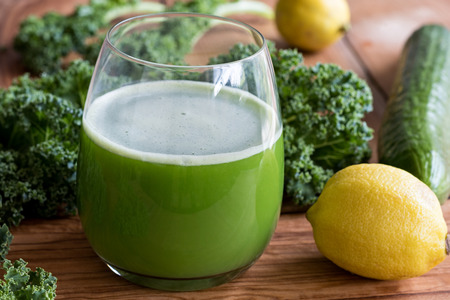 Green juice with kale, cucumber and lemon in a glass on a wooden tableの写真素材