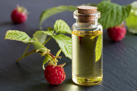 A bottle of raspberry seed oil with raspberries on a dark backgroundの写真素材