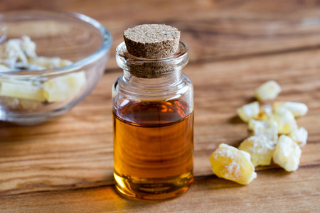 A bottle of frankincense essential oil with frankincense resin crystals in the background, on a wooden tableの写真素材
