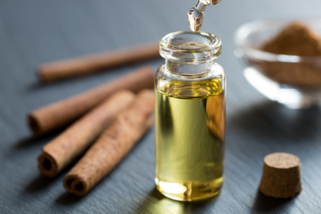 A drop of cinnamon essential oil is being dropped into a bottle, with cinnamon sticks and powder in the backgroundの写真素材