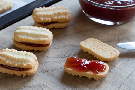 Filling Christmas cookies with strawberry jam on a wooden cutting boardの写真素材