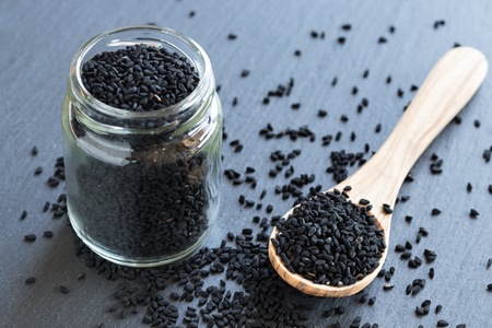 Black cumin seeds on a wooden spoon and in a glass jarの写真素材