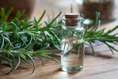 A bottle of rosemary essential oil with rosemary twigs on a wooden backgroundの写真素材
