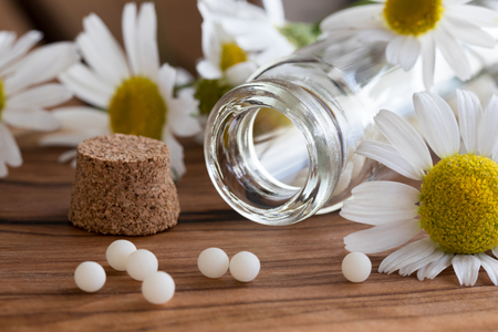 A bottle of homeopathic pills with chamomile flowers on a wooden tableの写真素材