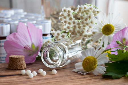 A bottle of homeopathic pills with chamomile, yarrow and other flowers on a wooden tableの写真素材