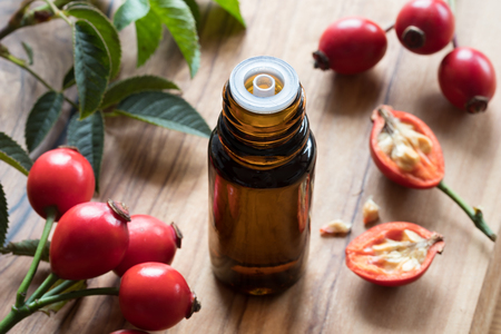 A bottle of rosehip seed oil on a wooden table, with fresh rosehips in the backgroundの写真素材