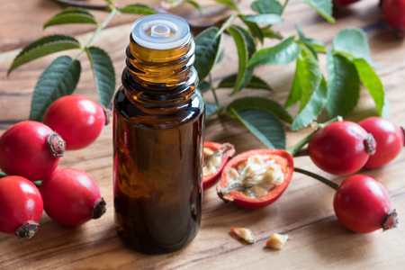 A bottle of rosehip seed oil on a wooden table, with fresh rosehips in the backgroundの写真素材