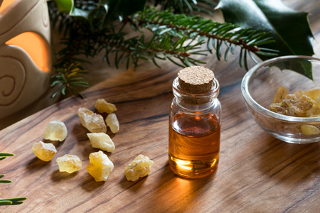 A bottle of frankincense essential oil with frankincense resin crystals, spruce and holly branches, and an aroma lamp in the backgroundの写真素材