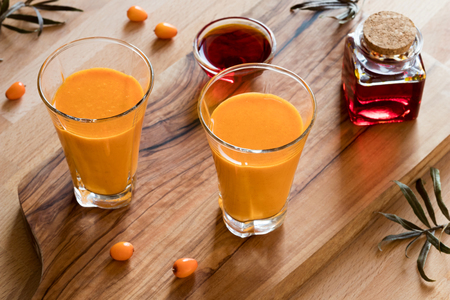 Two glasses of sea buckthorn juice, with sea buckthorn oil and berries in the backgroundの写真素材