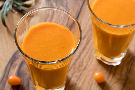 Two glasses of sea buckthorn juice with sea buckthorn berries in the backgroundの写真素材