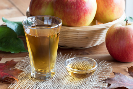 Apple cider vinegar in a glass, with apples and autumn leaves in the backgroundの写真素材