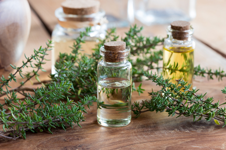 A bottle of thyme essential oil on a wooden table, with fresh thyme twigs and bottles in the backgroundの写真素材