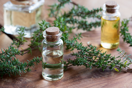 A bottle of thyme essential oil on a wooden table, with fresh thyme twigs and other bottles in the backgroundの写真素材