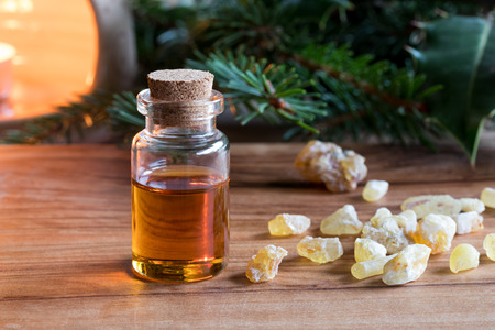 A bottle of frankincense essential oil with frankincense resin, spruce and holly branches, and an aroma lamp in the backgroundの写真素材