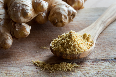 Ground ginger on a wooden spoon, with fresh ginger root in the backgroundの写真素材