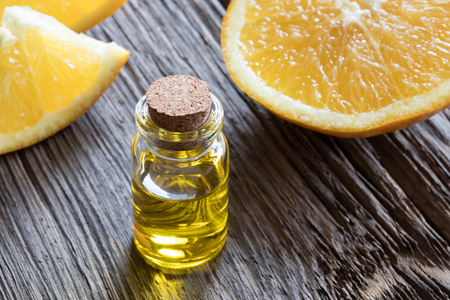 A bottle of orange essential oil on a wooden table, with fresh orange wedges in the backgroundの写真素材