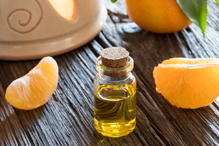 A bottle of tangerine essential oil on a wooden table, with tangerines and an aroma lamp in the backgroundの写真素材