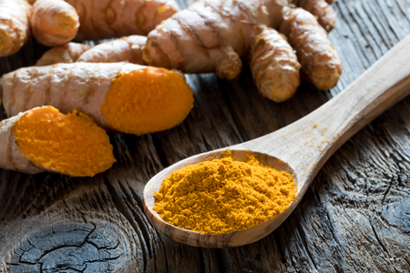 Ground turmeric on a wooden spoon, with fresh turmeric root in the backgroundの写真素材