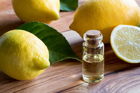 A bottle of lemon essential oil on a wooden table, with lemons in the backgroundの写真素材
