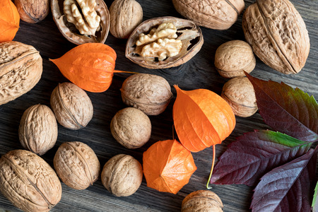 Whole and broken walnuts, Physalis (Chinese lantern) and autumn leaves on a wooden table, top viewの写真素材