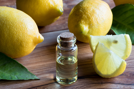 A transparent bottle of lemon essential oil on a wooden table, with whole lemons and lemon wedges in the backgroundの写真素材