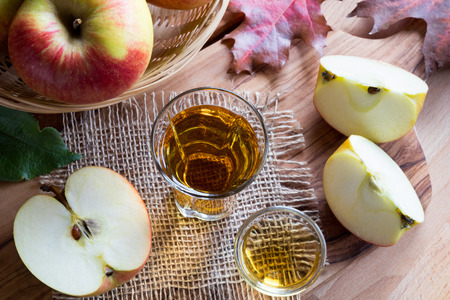 Apple cider vinegar in a glass, with apples and autumn leaves in the backgroundの写真素材