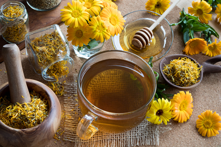 A cup of calendula (marigold) tea on a table, with fresh and dry calendula flowers in the backgroundの写真素材