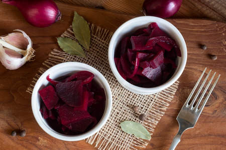 Fermented red beet with onions in two round bowls, with garlic, purple onions, allspice and bay leaf in the background, top viewの写真素材