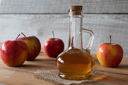 A bottle of apple cider vinegar on a wooden table, with apples in the backgroundの写真素材