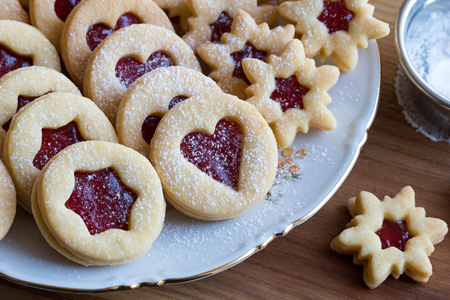 Traditional Linzer Christmas cookies filled with strawberry jam and dusted with sugar, arranged on a plate on a wooden tableの写真素材