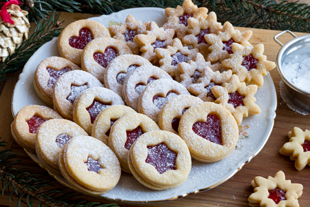 Linzer Christmas cookies filled with strawberry jam and dusted with sugar, arranged on a plate on a wooden tableの写真素材