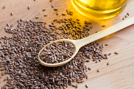 Flaxseeds on a wooden spoon, with flax seed oil in the backgroundの写真素材