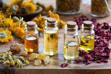 Bottles of essential oil with dried rose petals, chamomile, calendula and frankincense resin on a wooden backgroundの写真素材
