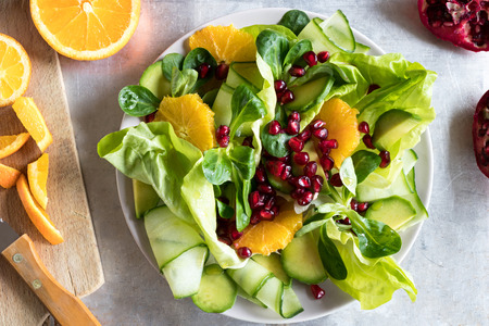 Fruit and vegetable salad on a bright metal background, top view. Lettuce, corn salad, cucumber, avocado, orange, pomegranate.の写真素材