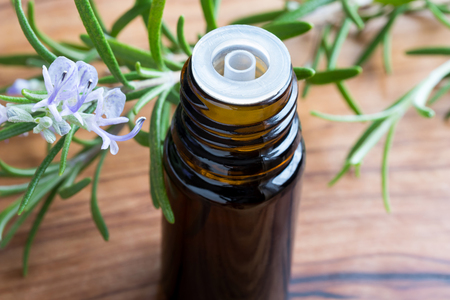 A dark bottle of rosemary essential oil with fresh blooming rosemary twigs on a wooden backgroundの写真素材