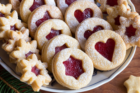 Linzer Christmas cookies filled with strawberry jam and dusted with sugar, arranged on a plateの写真素材