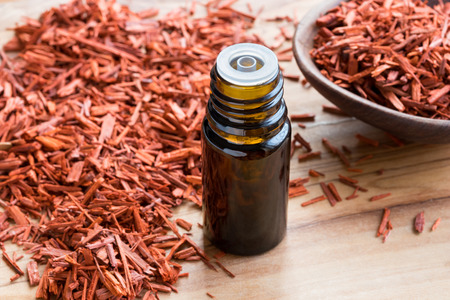 A bottle of sandalwood essential oil on a wooden table, with sandalwood in the backgroundの写真素材