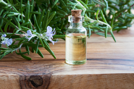 A bottle of rosemary essential oil with fresh blooming rosemary twigs on a wooden tableの写真素材