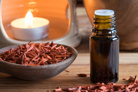 A bottle of sandalwood essential oil with sandalwood pieces and an aroma lamp in the backgroundの写真素材