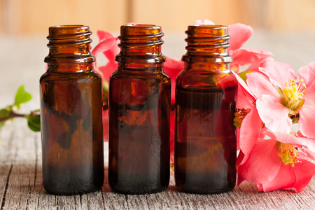 Three bottles of essential oil with red blossoms in the backgroundの写真素材