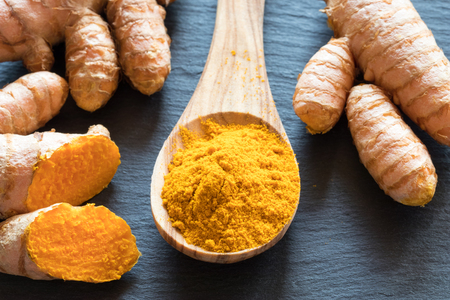 Turmeric powder and fresh turmeric root on a dark backgroundの写真素材
