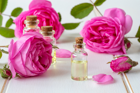 A bottle of essential oil with roses on a white wooden tableの写真素材