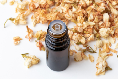 A bottle of essential oil with dried jasmine flowers on a white backgroundの写真素材