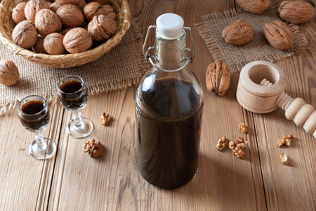 A bottle of homemade nut liqueur with walnuts on a tableの写真素材