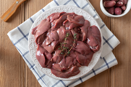 Fresh raw chicken livers on a plate and hearts in a bowl, top viewの写真素材