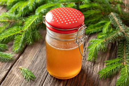 A jar of homemade herbal syrup against cough made from young spruce tips on a tableの写真素材