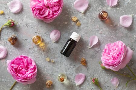Bottles of essential oil with frankincense resin and rose de mai flowers on a grey background