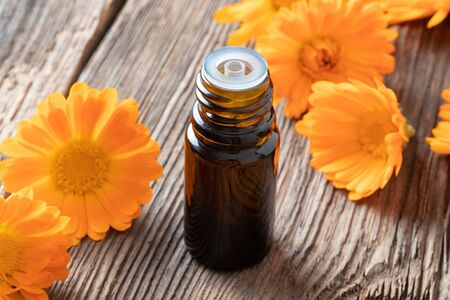 A bottle of essential oil with fresh calendula flowers on a tableの写真素材