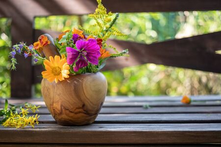 Calendula, mallow, goldenrod and other medicinal herbs in a wooden mortar in a gardenの写真素材