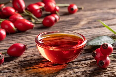 A bowl of rose hip seed oil with fresh rose hipsの写真素材